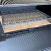 Expanded grate screen sits in the bottom of a firebox of a wood grill for airflow.