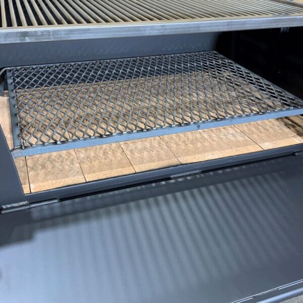Expanded grate screen sits in the bottom of a firebox of a wood grill for airflow.